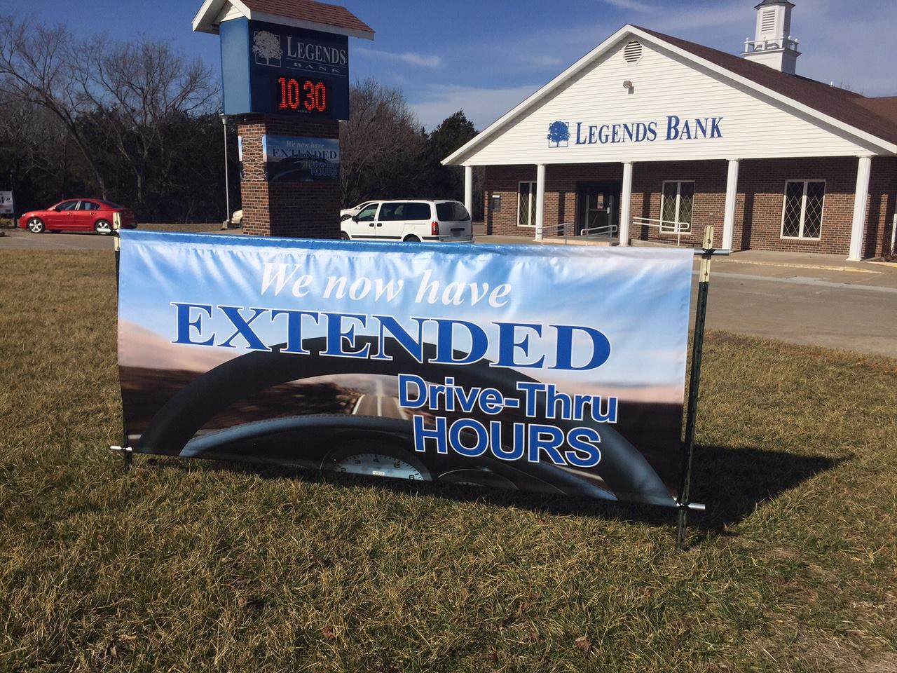 Vinyl banner announcing extended drive-thru hours stretched in front of a bank building